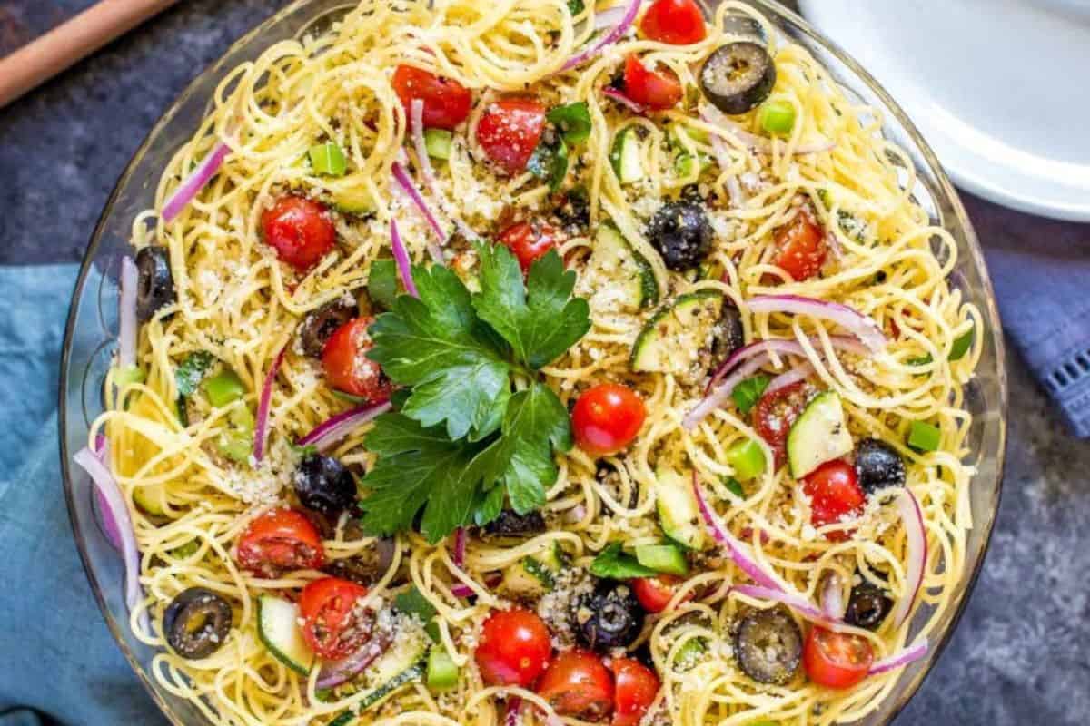 A crowd-pleasing bowl of spaghetti salad with cherry tomatoes, olives, red onion, green bell peppers, zucchini, and a parsley garnish, making it perfect for any potluck gathering.