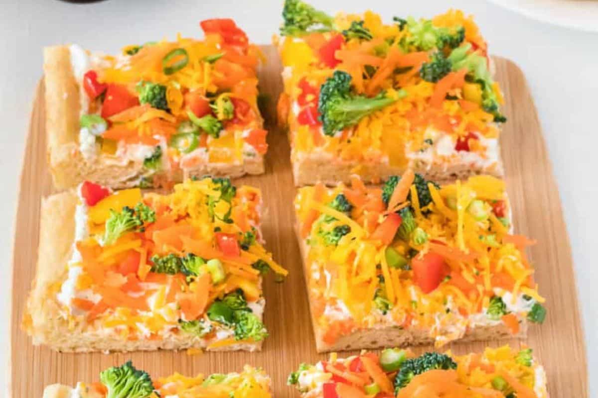 Six square slices of colorful vegetable pizza on a wooden board, topped with broccoli, carrots, tomatoes, and cheese—a must-try for the perfect night in.