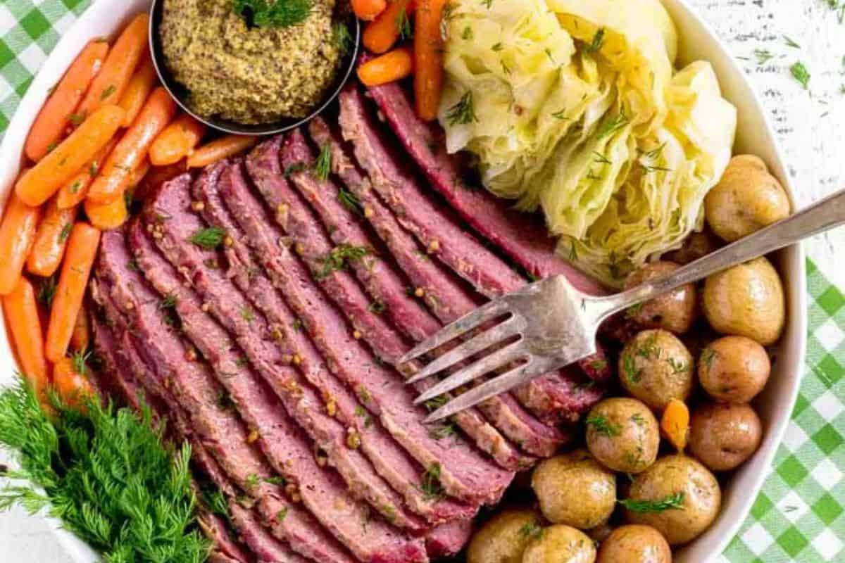 A plate of sliced corned beef with carrots, cabbage, and potatoes, accompanied by a dish of mustard and garnished with dill. This Irish-inspired comfort food is perfect to warm your soul.