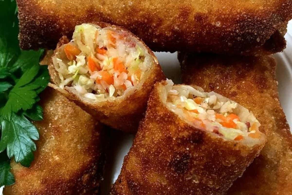 Close-up of crispy egg rolls filled with chopped vegetables and tender corned beef, stacked on a plate. Fresh parsley garnish on the side.