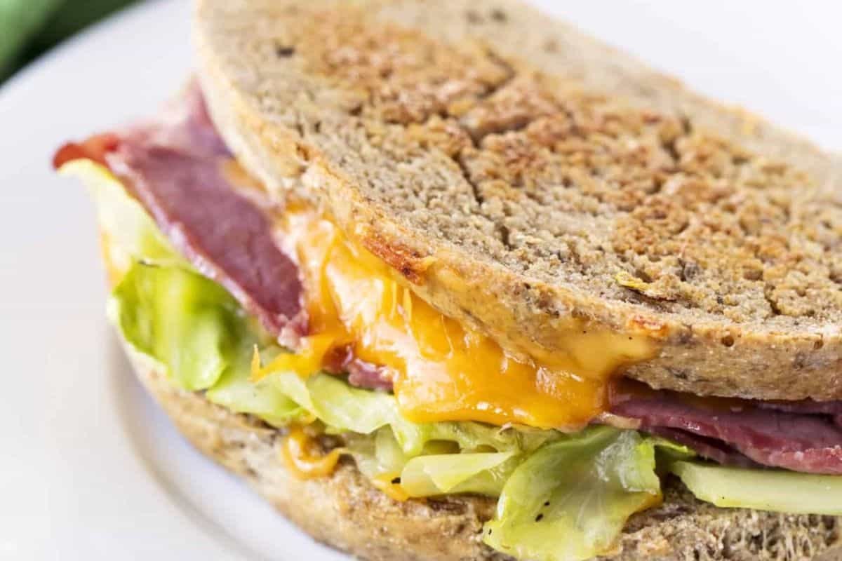 A toasted sandwich with melted cheese, crisp lettuce, and savory corned beef on rye bread sits invitingly on a white plate.