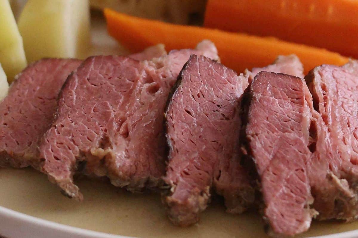 Warm your soul with this Irish-inspired dish: slices of cooked corned beef on a plate, complemented by comforting sides of carrots and potatoes in the background.