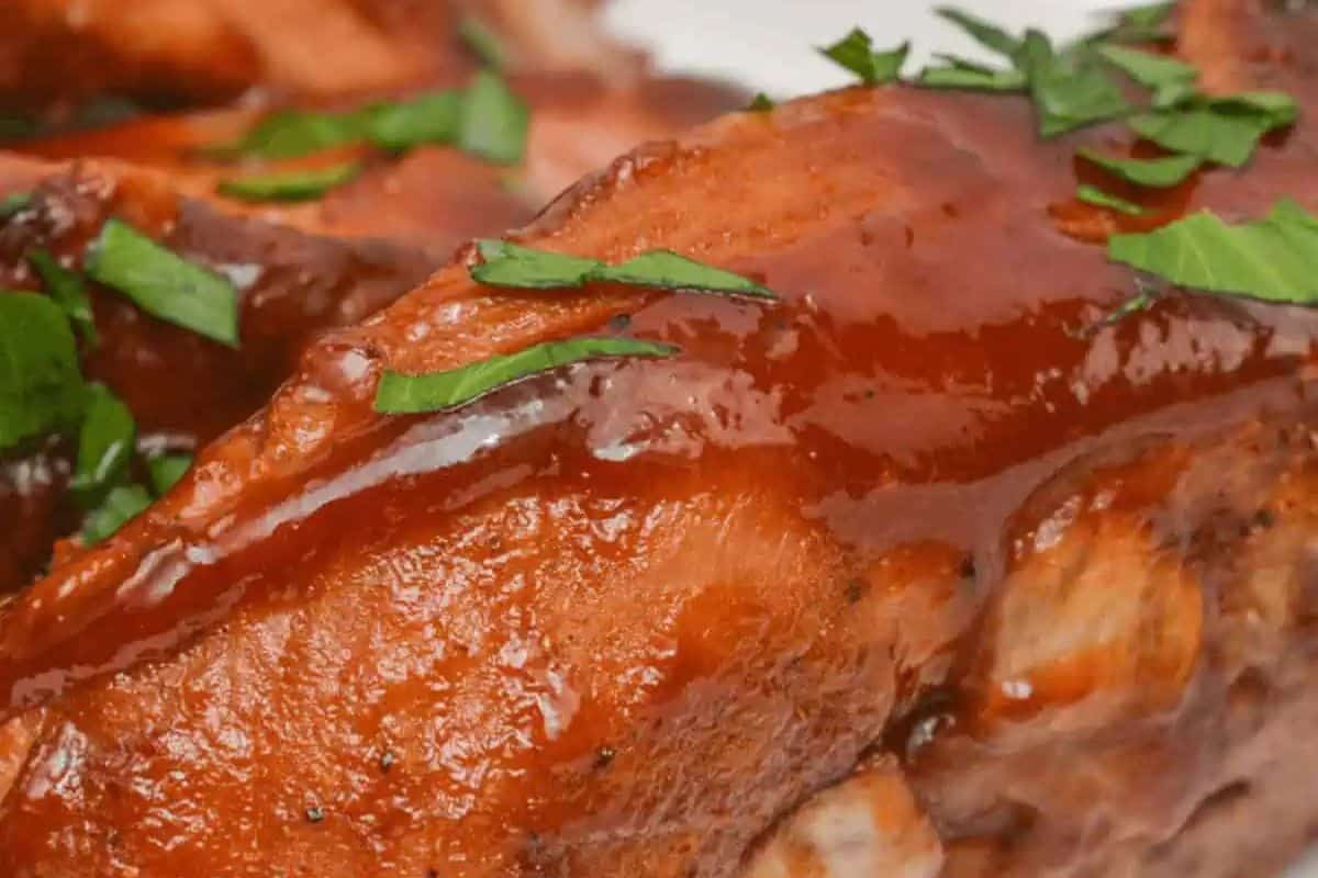 Close-up of barbecued ribs glazed with sauce and garnished with chopped fresh herbs—perfect for easy dinner recipes or slow cooker recipes.