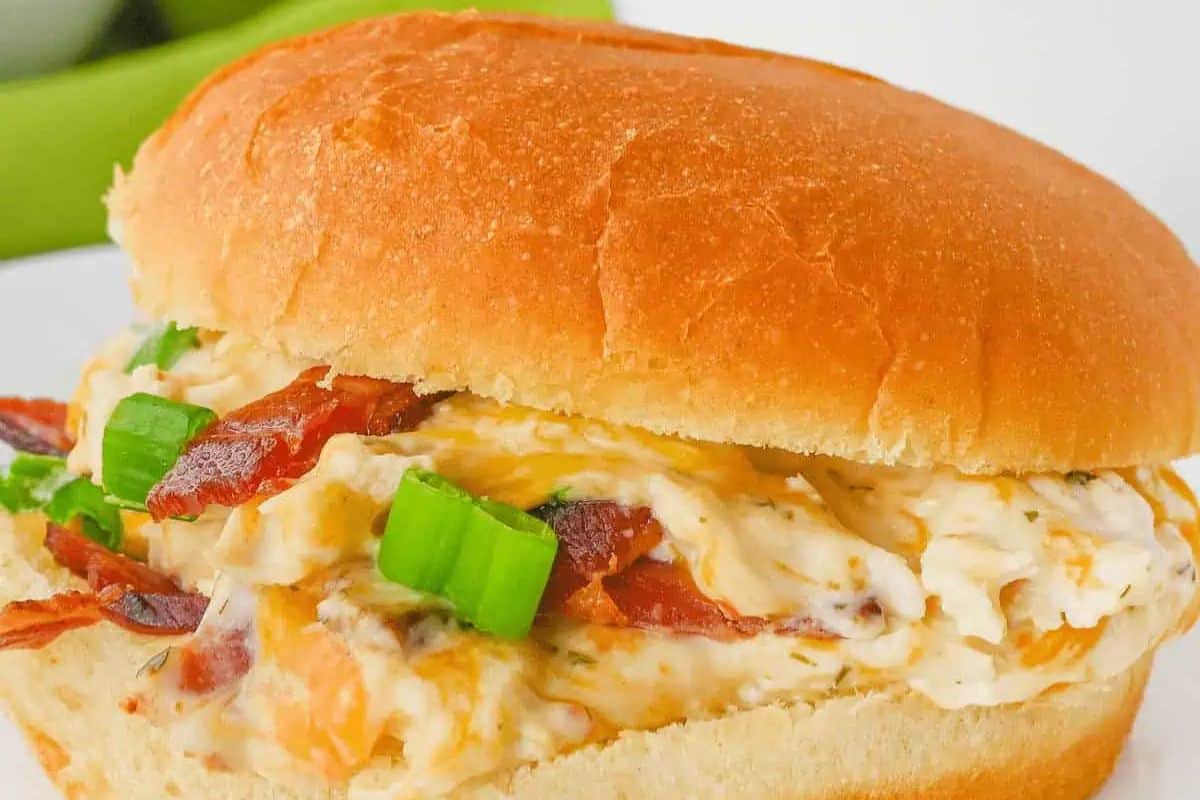 Close-up of a crowd-pleasing cracked chicken sandwich with a creamy filling, bacon, and green onions, nestled in a soft bun.