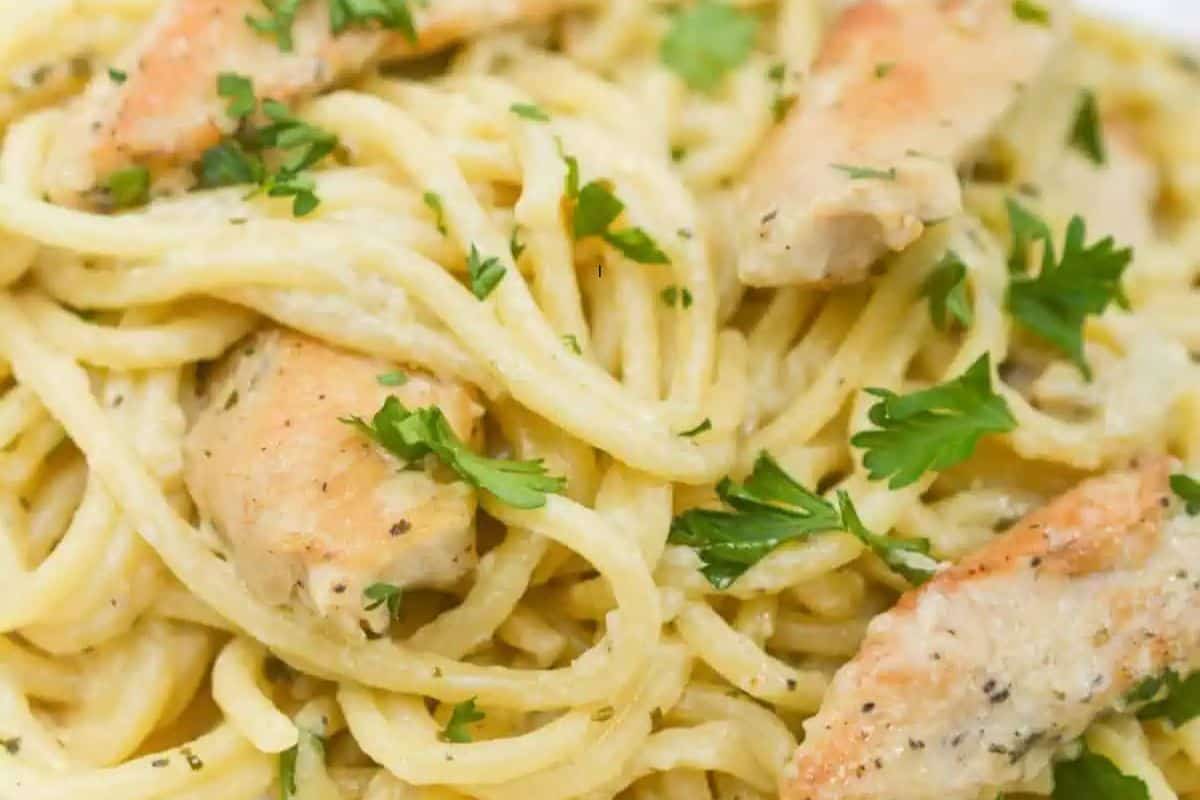 Close-up of chicken pasta with a creamy pesto sauce and fresh parsley.