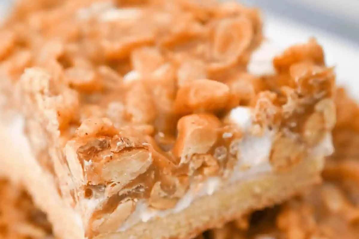 Close-up of a crunchy peanut butter bar with a crispy, golden-brown topping over a white layer, resembling the allure of blondies, set on a light-colored base.