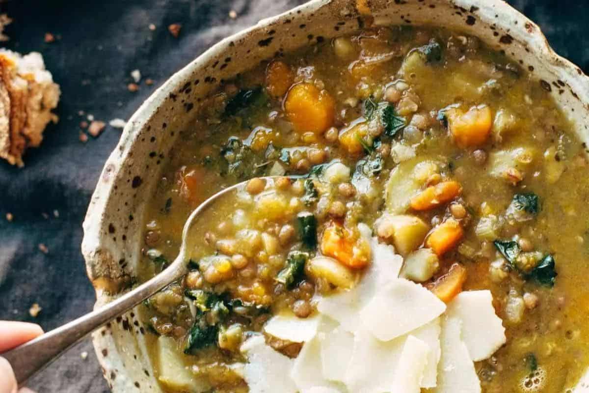 A close-up of a bowl of lentil soup with vegetables and leafy greens, topped with shaved cheese and a spoon inside the bowl—one of many easy Weight Watchers recipes perfect for a nutritious meal.