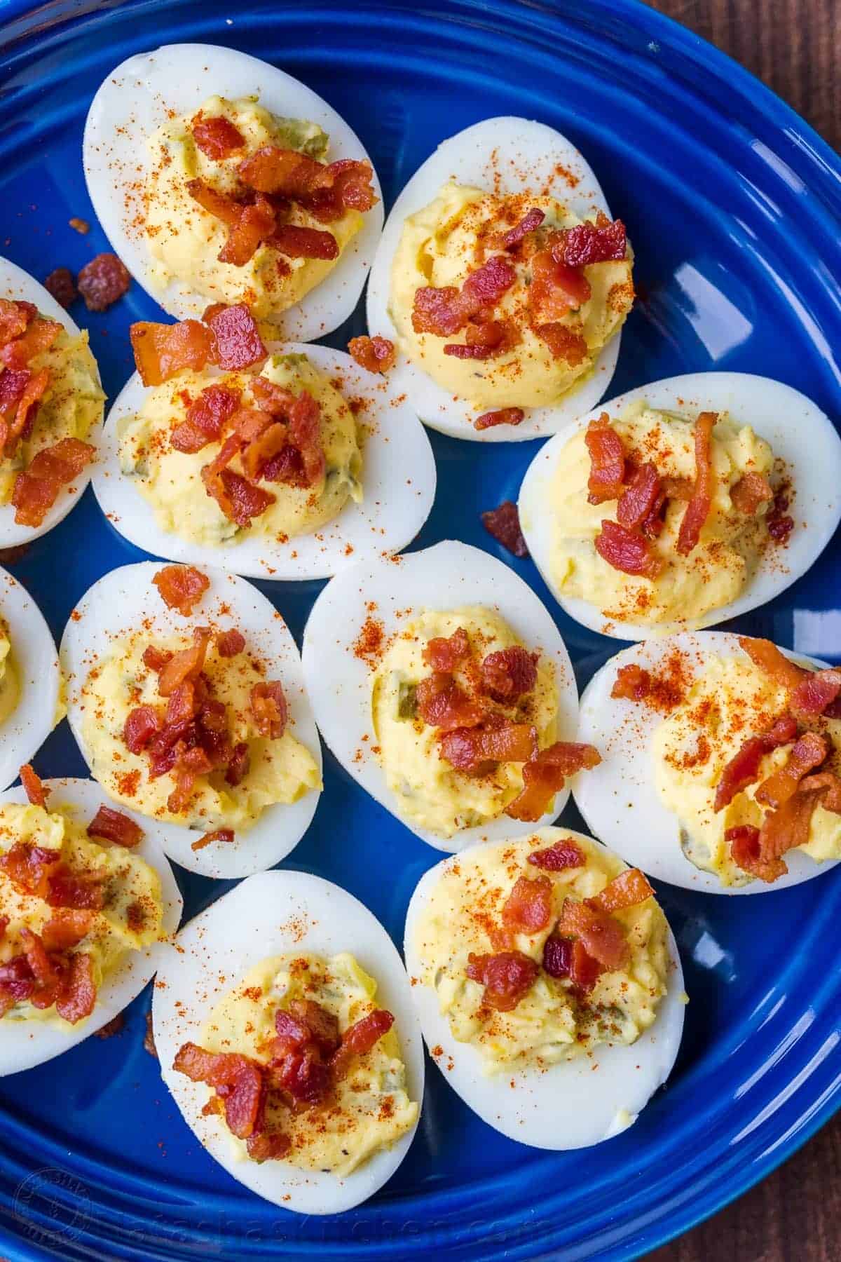 Deviled eggs, topped with crumbled bacon and a sprinkle of paprika, make for foolproof potluck dishes when served on a blue plate.