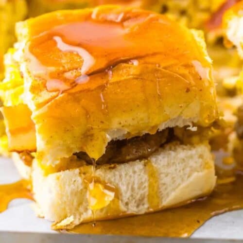 Start your day with a mouthwatering brunch slider featuring crispy bacon, fluffy eggs, and savory sausage on a bun, all topped with a drizzle of maple syrup.