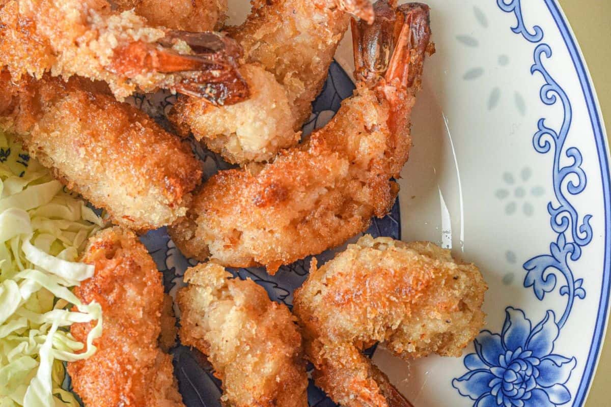 Enjoy a taste of restaurant-quality dining at home with our fried shrimp, featuring a perfectly crispy coating. Served on a decorative plate, it's paired with a side of fresh shredded cabbage for the ultimate shrimp dish experience.