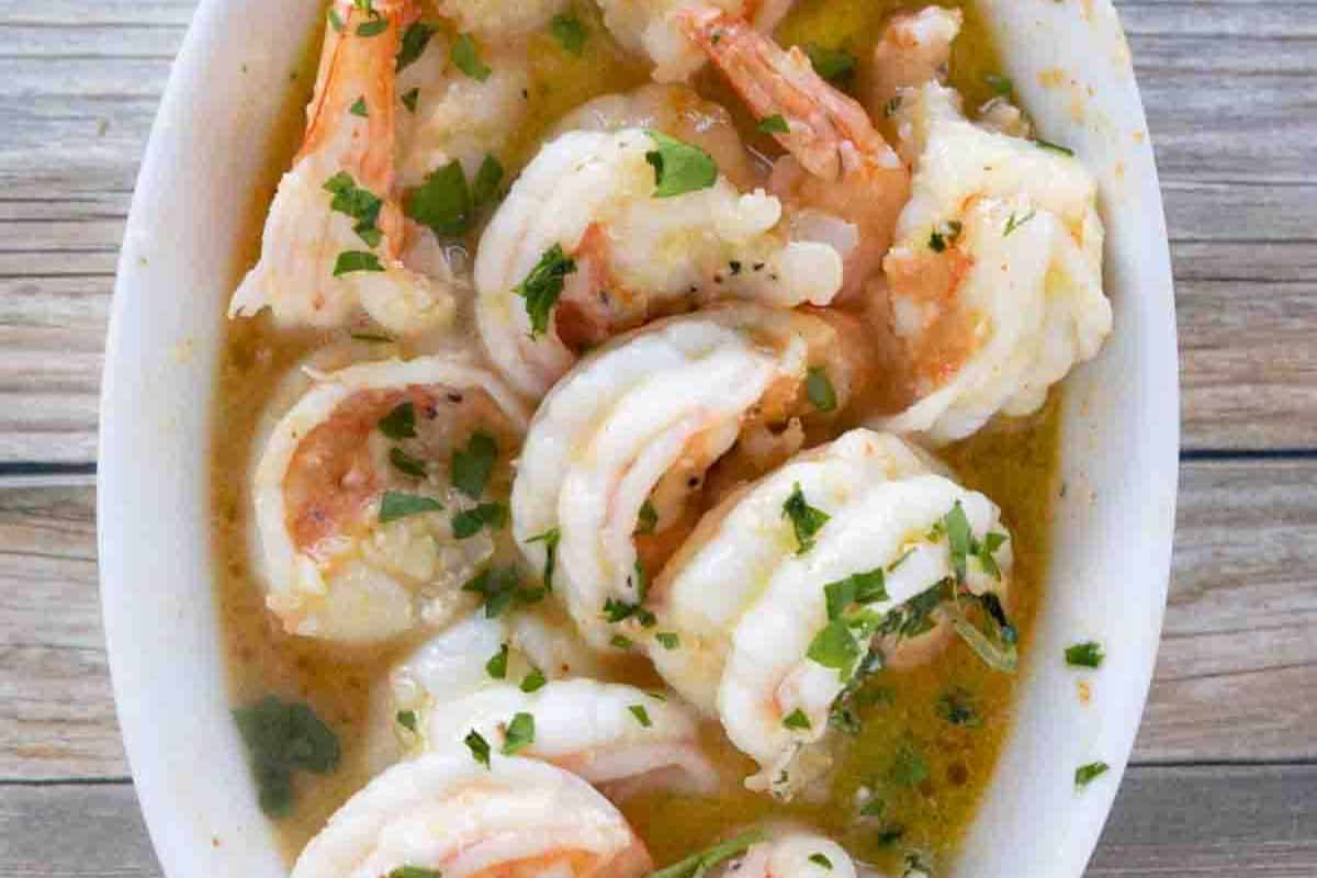 Enjoy a restaurant-quality dish of shrimp, perfectly garnished with chopped parsley and served in a rich garlic butter sauce, all elegantly presented on a wooden table.