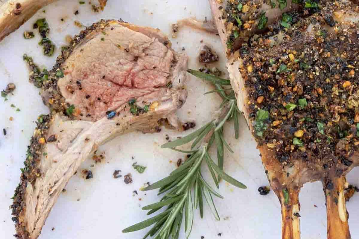 Close-up of a rack of lamb with a seasoned crust, garnished with rosemary.