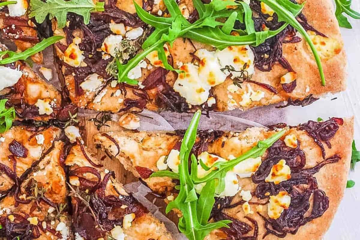This must-try pizza, perfect for a night in, is topped with caramelized onions, goat cheese, and fresh arugula on a wooden board.