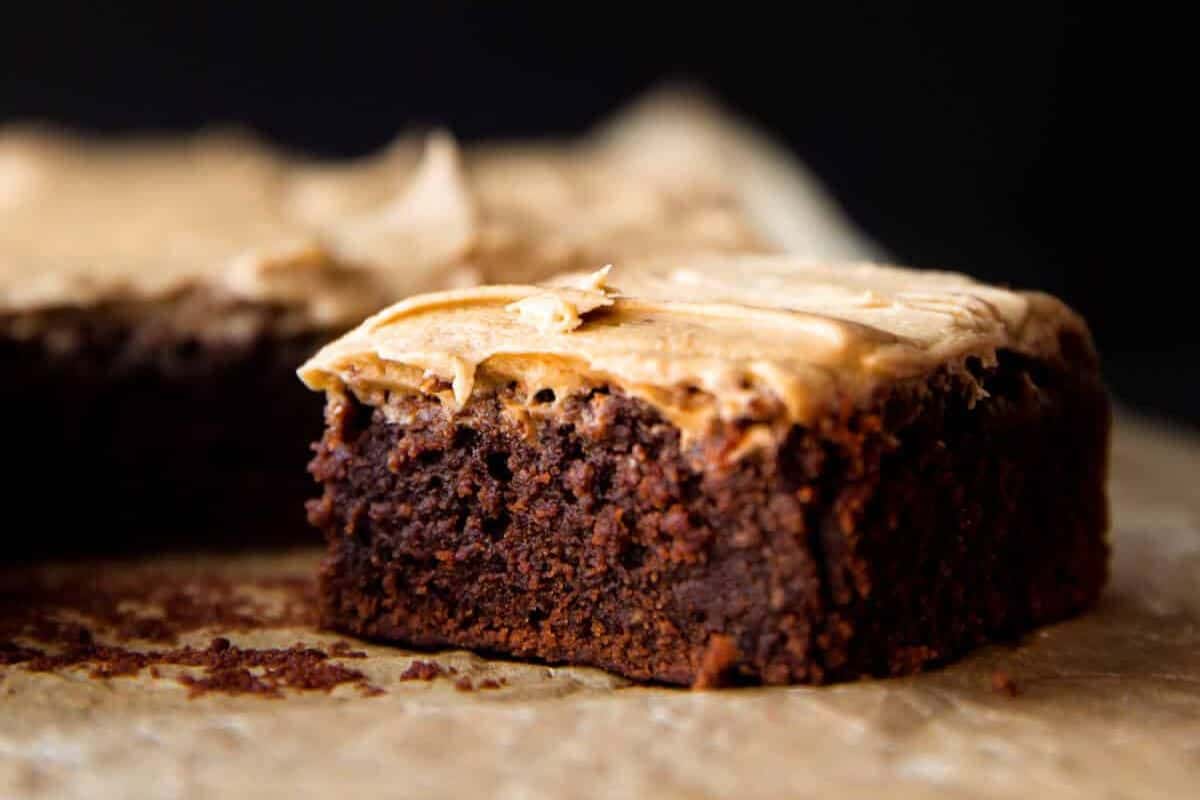 A cute close-up of a square chocolate brownie with light brown frosting on top, sitting sweetly on parchment paper, perfect for savoring St. Patrick's Day treats.