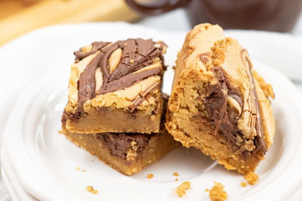Two sumptuous swirled chocolate and hazelnut blondies are stacked elegantly on a white plate, resembling a refined twist on traditional brownies. These delightful bars offer a perfect blend of rich flavors for an indulgent treat.