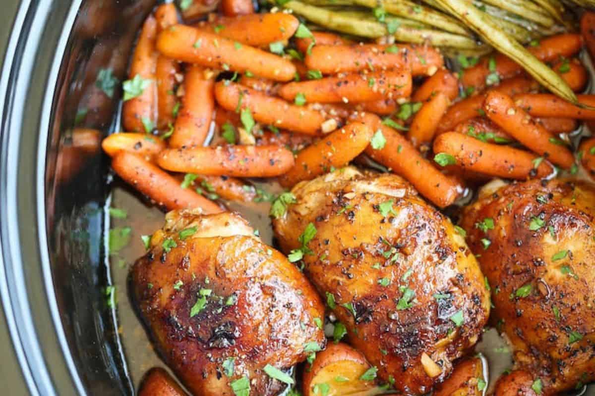 Tender chicken thighs with baby carrots and green beans, garnished with chopped herbs, simmer in a seasoned broth—an easy dinner perfect for busy nights. Try this flavorful meal from our collection of slow cooker recipes.