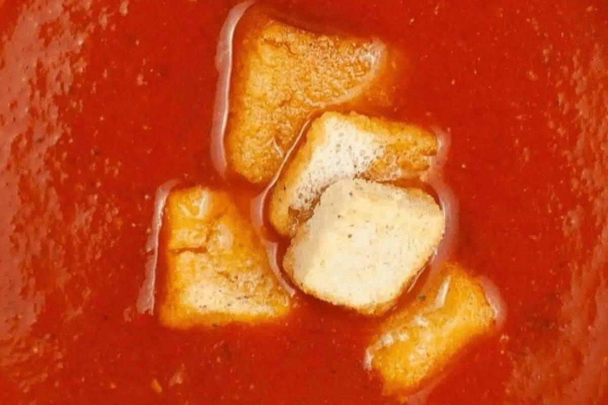 Extreme close-up of some red tomato soup, topped with croutons.