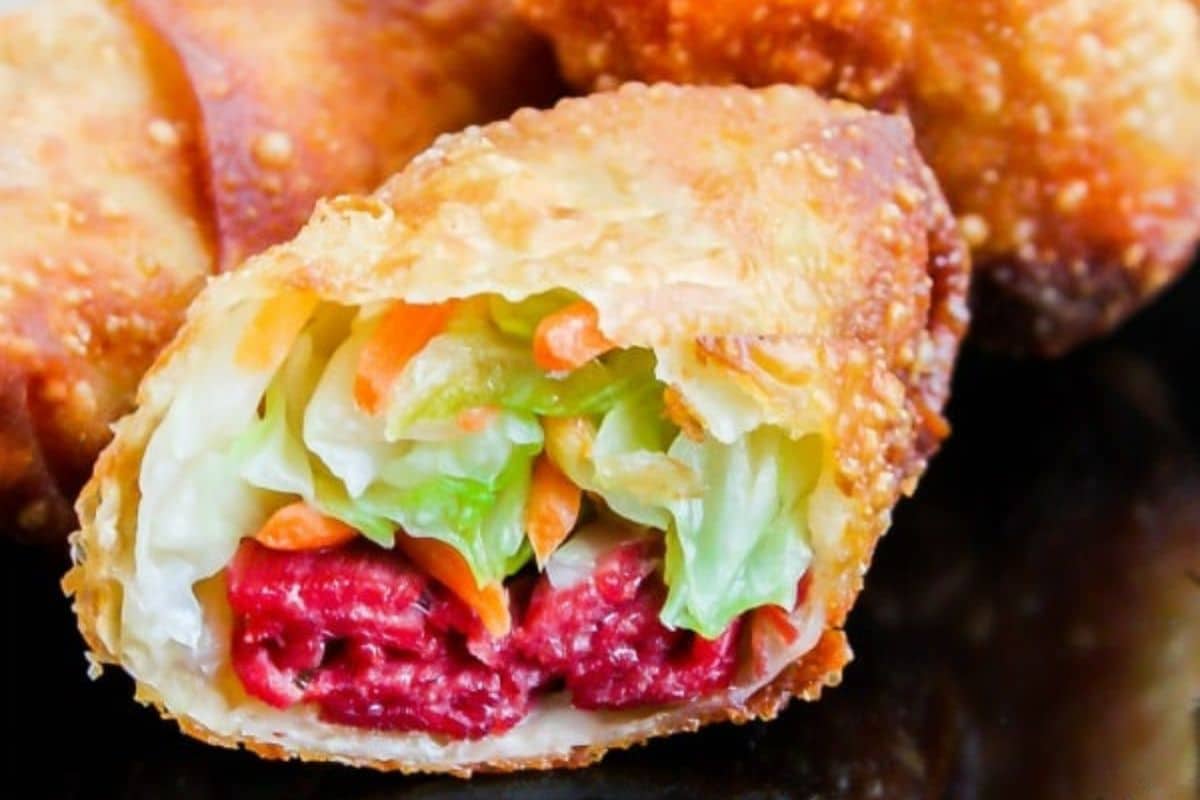 A close-up of a halved egg roll reveals its comforting filling of lettuce, carrots, and cooked red meat wrapped in a crispy brown shell. This Irish-inspired comfort food is sure to warm your soul with every bite.