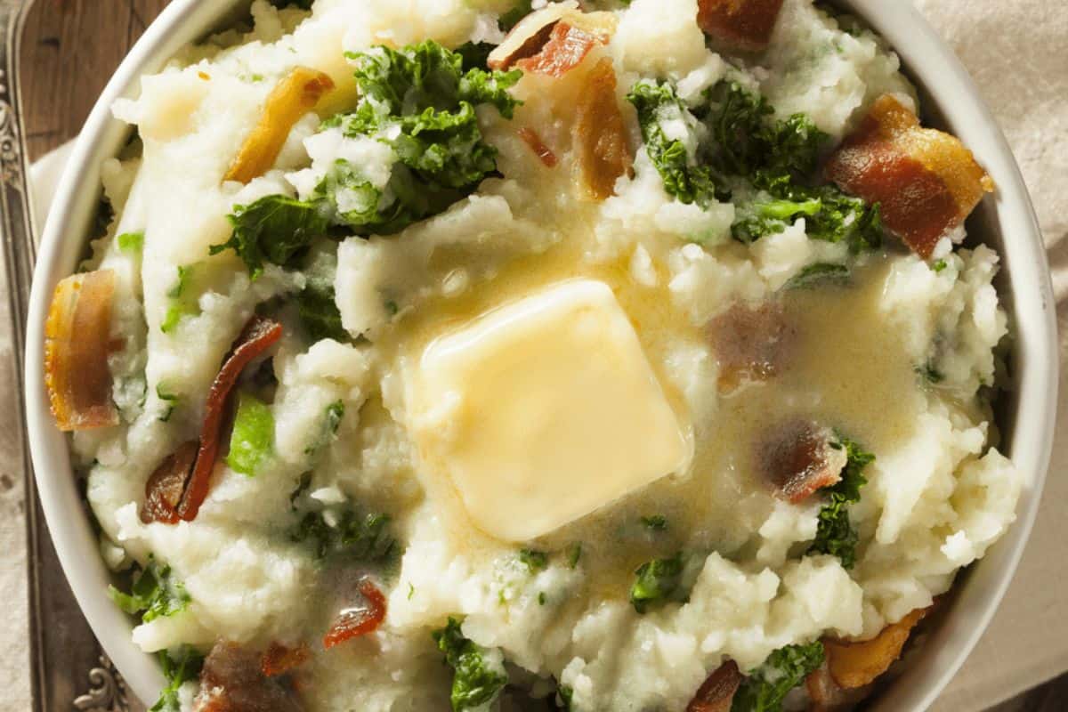 A bowl of Irish-Inspired mashed potatoes with kale and bacon bits, topped with melting butter.