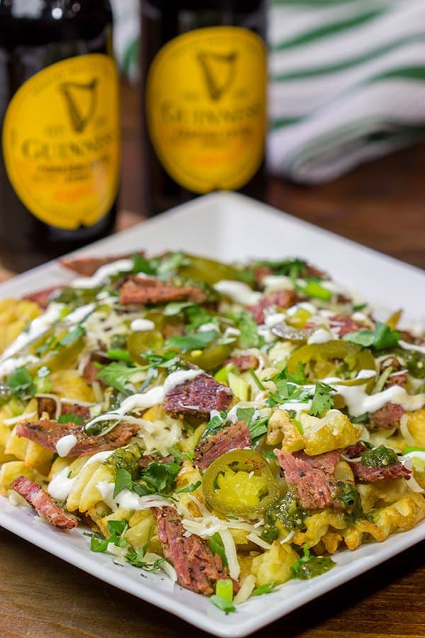 A plate of waffle fries topped with melted cheese, sliced meat, jalapeños, and drizzled sour cream makes for a perfect treat during St. Patrick’s Day celebrations. Two bottles of Guinness beer sit in the background, completing this Irish-inspired dinner delight.