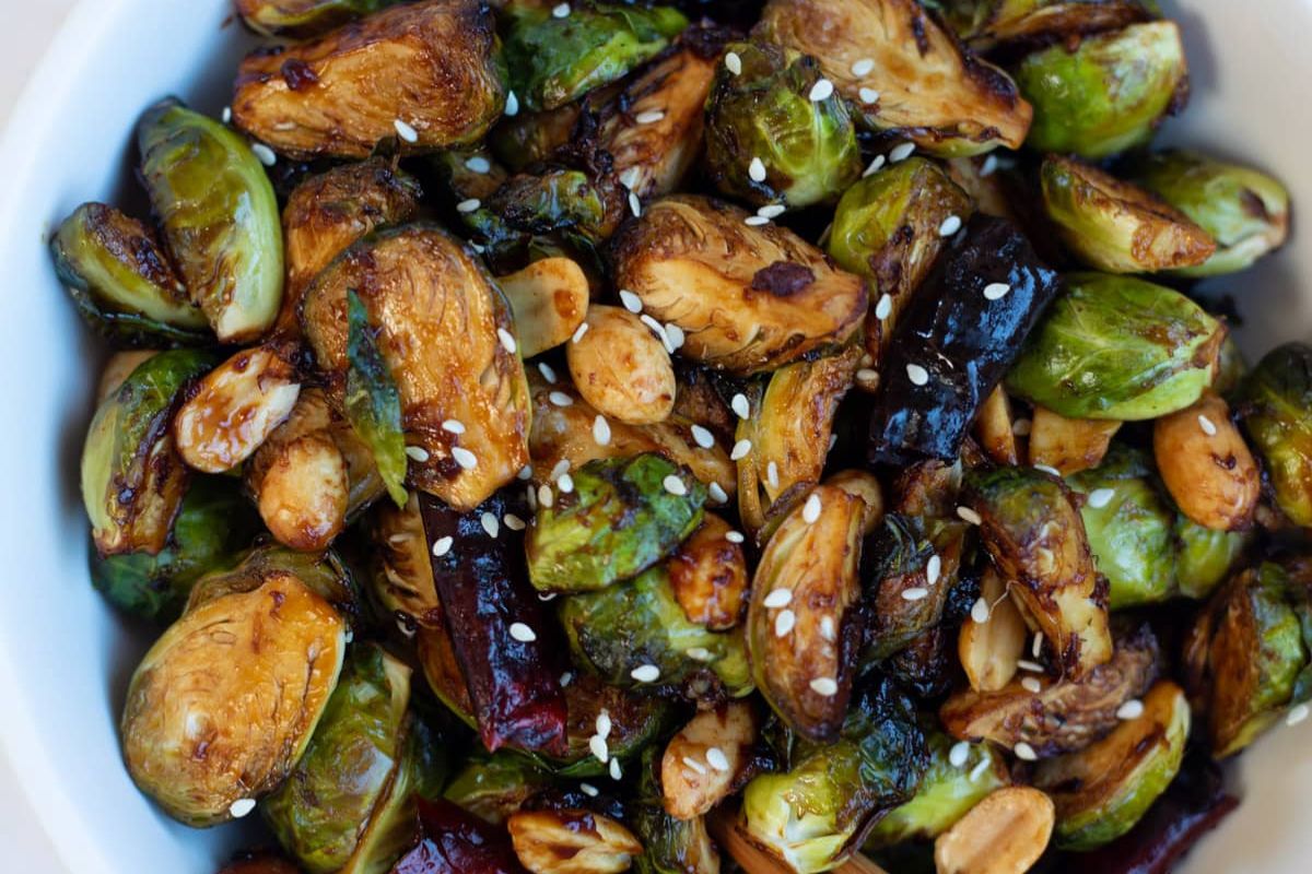 A bowl of roasted Brussels sprouts mixed with almonds and sprinkled with sesame seeds makes a crowd-pleasing dish perfect for potluck recipes.