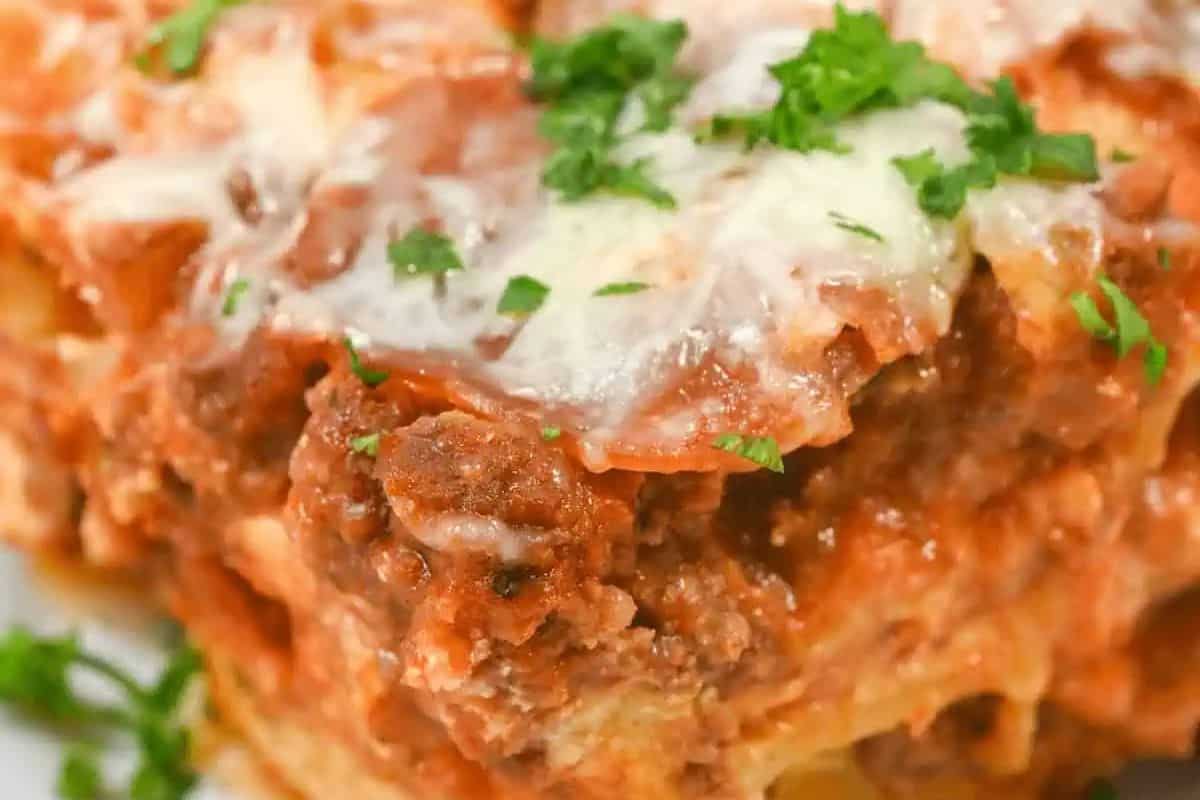 Close-up of a slice of lasagna topped with melted cheese, savory meat sauce, and garnished with chopped parsley—perfect for easy dinner or added to your favorite dinner recipes.