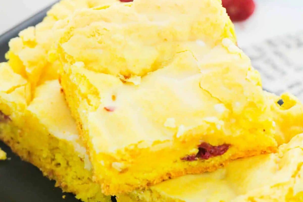 Two pieces of a yellow lemon blondie with raspberries rest on a black plate against a softly blurred background.