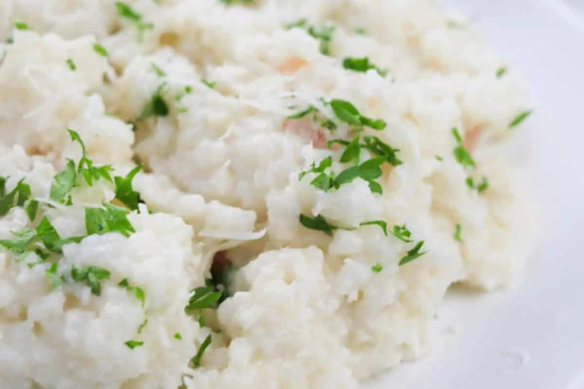 A close-up of restaurant-quality shrimp risotto, elegantly garnished with chopped green herbs on a pristine white plate.