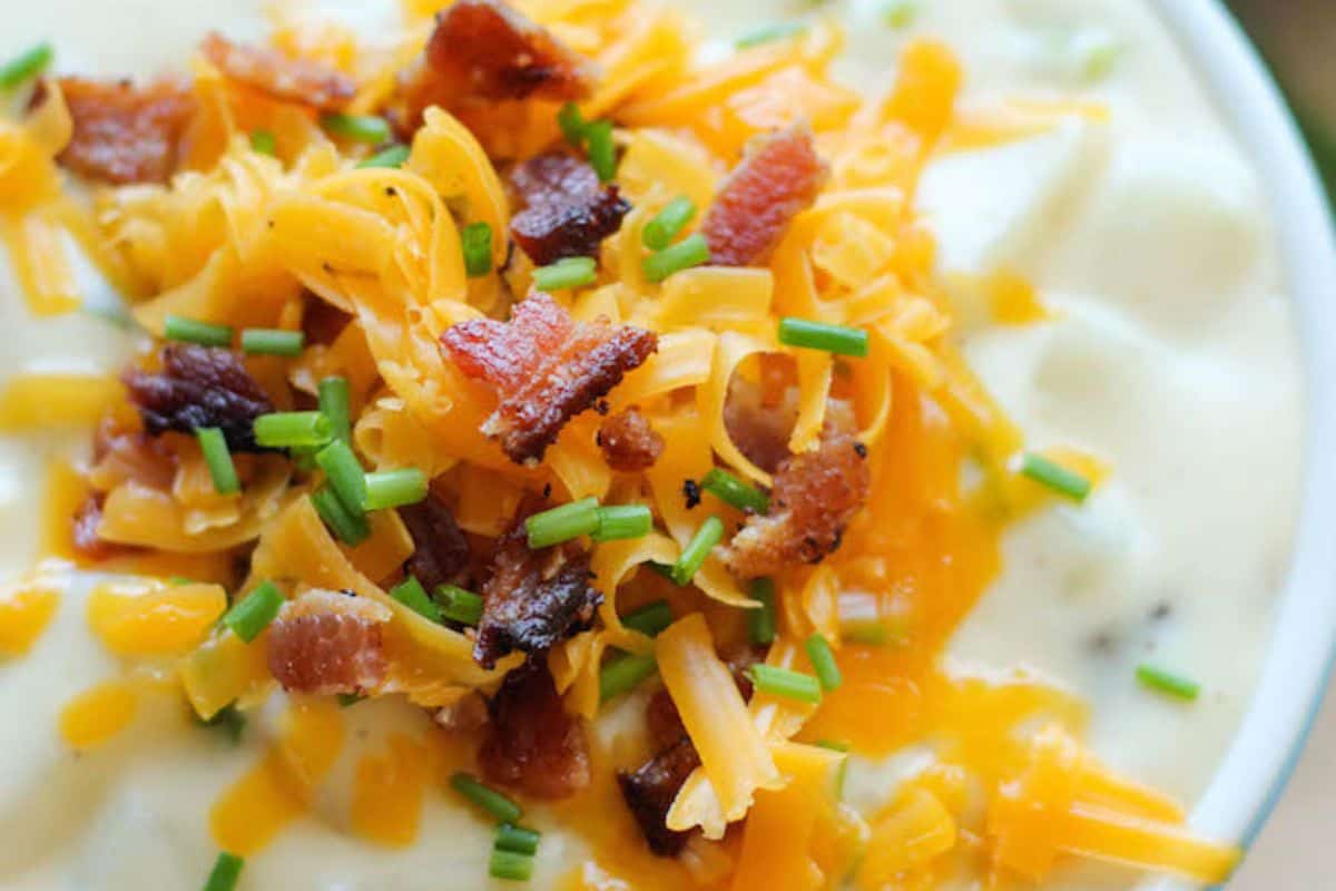 Close-up of a bowl of loaded baked potato soup, served in a white bowl and topped with cheese, bacon, and green onions.