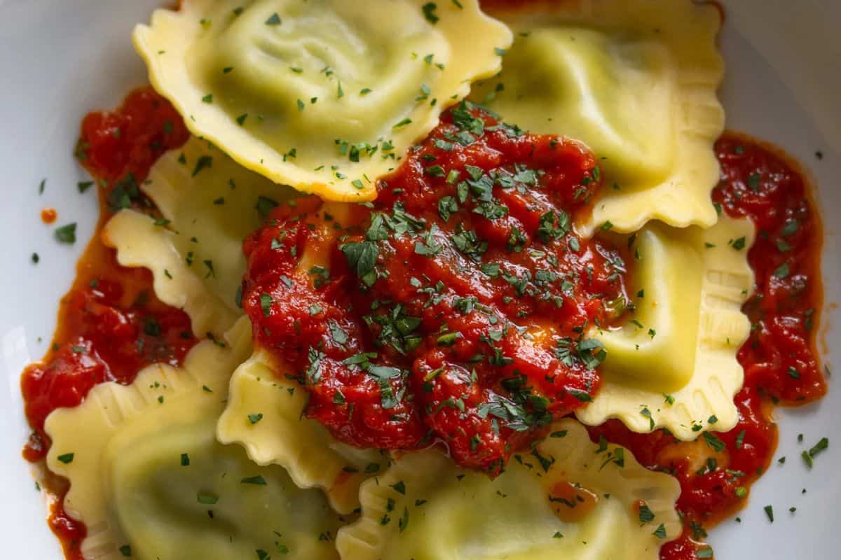 Close-up of lobster ravioli with a rich tomato sauce and chopped parsley.