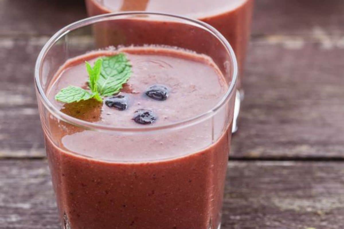 A glass of berry smoothie, inspired by Easy Weight Watchers Recipes, topped with a mint sprig and a few whole berries, placed on a wooden surface.