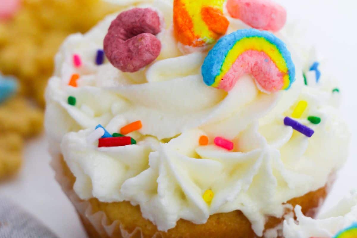 Celebrate with a delightful cupcake featuring white frosting, topped with colorful cereal pieces, including a festive rainbow shape, and multicolor sprinkles—perfect for adding a touch of whimsy to your St. Patrick's Day potluck recipes.