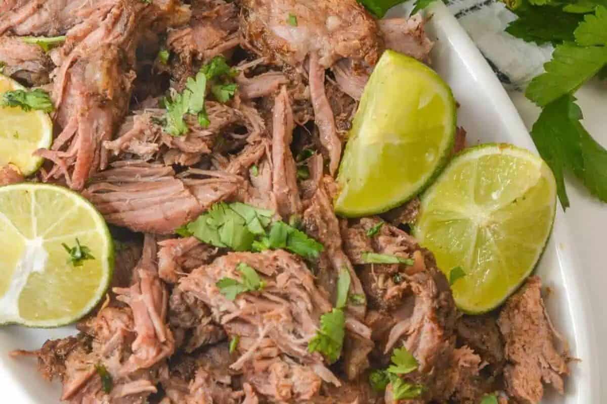 Shredded cooked meat garnished with chopped cilantro and served with lime wedges on a white plate—perfect for easy dinner nights and those who love simple dinner recipes.