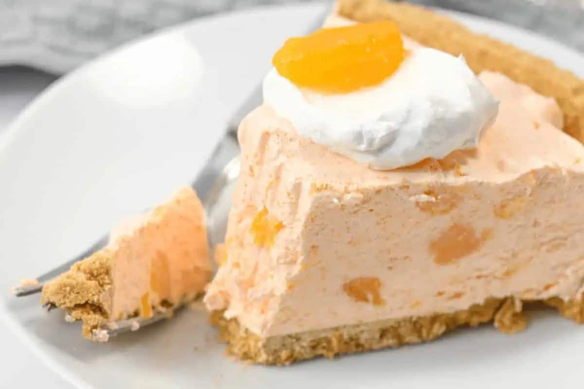 A slice of orange pie, one of those delightful no-bake treats, sits on a plate with whipped cream elegantly atop. A fork holds a bite beside it, tempting you into the easy desserts dessert game.