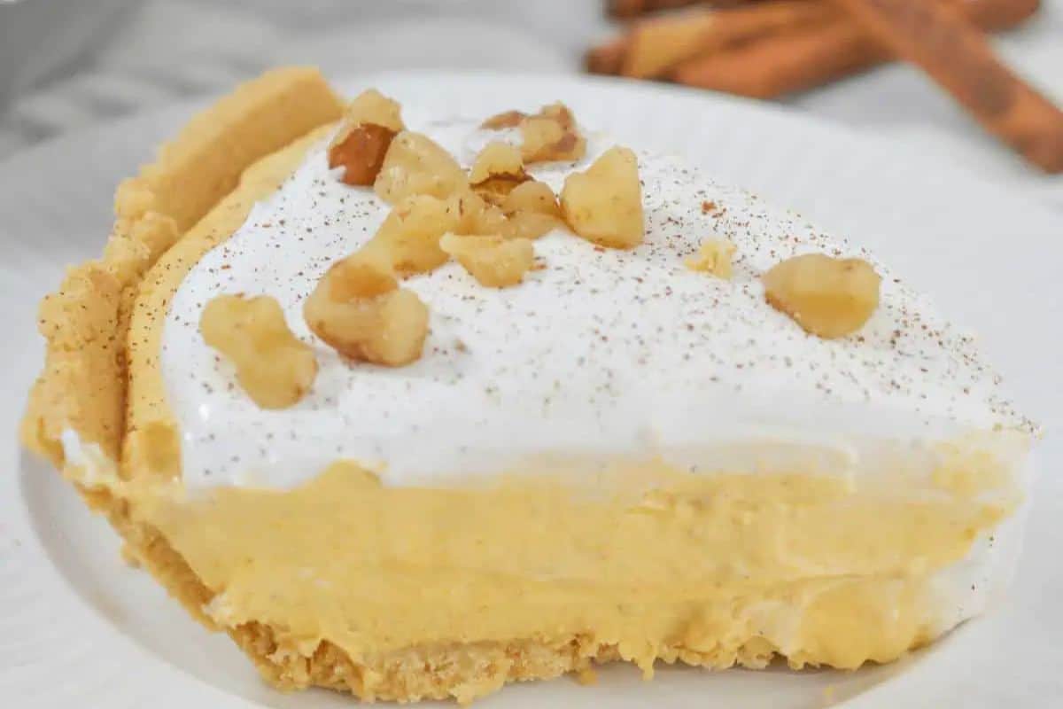 A slice of creamy pumpkin pie cheesecake, one of those irresistible easy desserts, is topped with whipped cream and chopped nuts, set on a white plate.