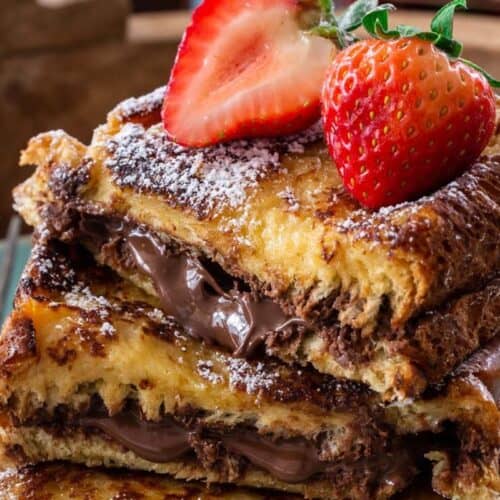 Two slices of French toast filled with chocolate spread, stacked on a plate, topped with halved strawberries and a dusting of powdered sugar—a perfect Valentine’s Day breakfast for those who love sweet and savory brunch recipes.