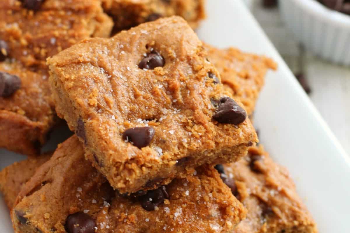 Close-up of peanut butter chocolate chip blondies stacked on a plate. The bars have a textured surface with visible chocolate chips and a sprinkle of salt.