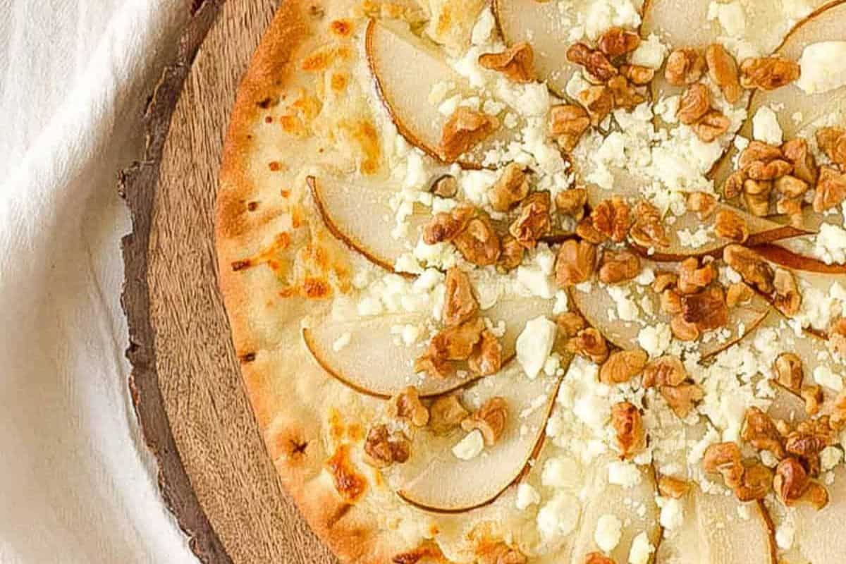 Perfect for a cozy night in, this must-try pizza is topped with pear slices, crumbled cheese, and walnuts on a wooden board. It's an irresistible combination that's sure to elevate your pizza recipes collection.