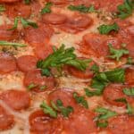Close-up of a pepperoni pizza topped with melted cheese and garnished with fresh parsley leaves, reminiscent of the flavors found in a classic Pepperoni Dip.