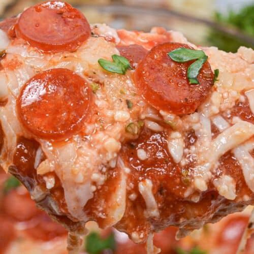 A close-up of a cheesy pizza slice topped with mini pepperoni slices and garnished with fresh herbs, the cheese stretching as it's lifted—reminiscent of a warm, savory Pepperoni Dip in pizza form.
