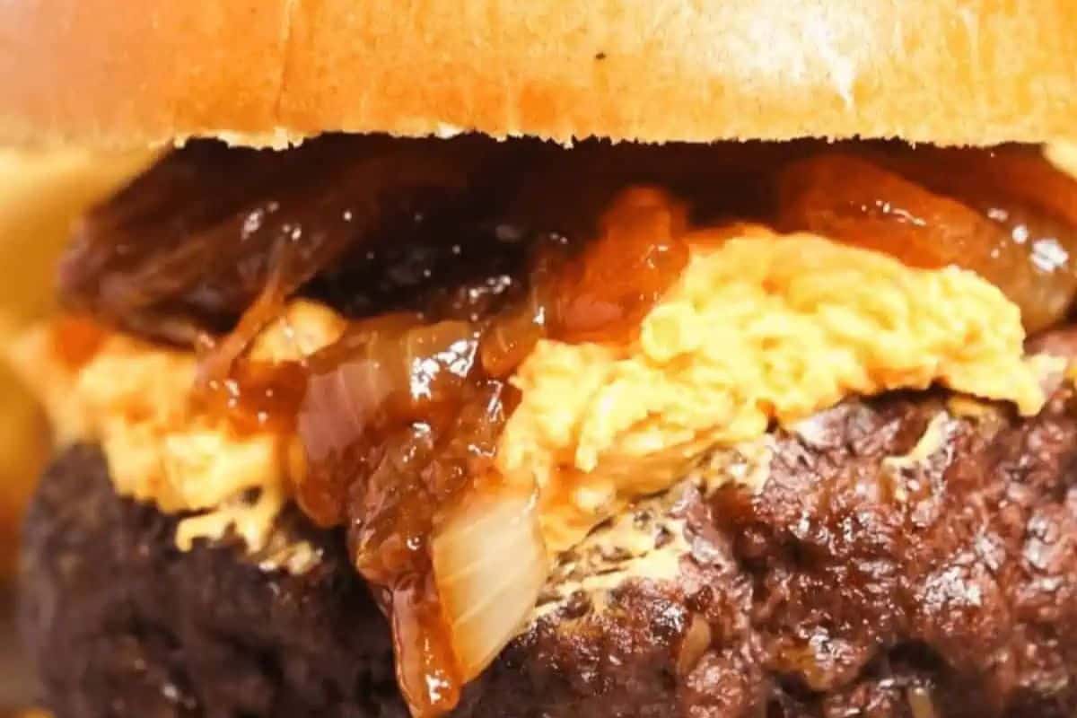 Close-up of a burger with a thick beef patty, beer cheese, and caramelized onions inside a bun—a true comfort food that will warm your soul with every bite.