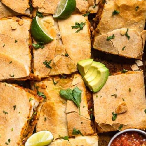A baking sheet with sliced quesadillas, garnished with lime wedges, avocado slices, cilantro, and a small bowl of salsa on the side—perfect for Sheet Pan Meals that promise delicious flavors and easy cleanup.
