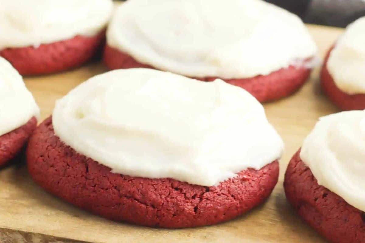 Red velvet cookies with cream cheese frosting are displayed on a wooden surface, perfect for Galentine's Day celebrations.