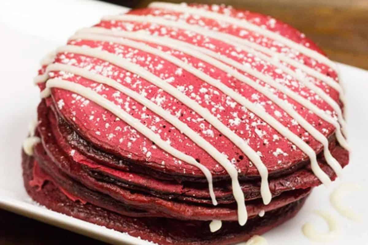 A stack of red velvet pancakes topped with powdered sugar and drizzled with white icing on a white plate—perfect for sweet and savory brunch recipes or a special Valentine's Day breakfast.