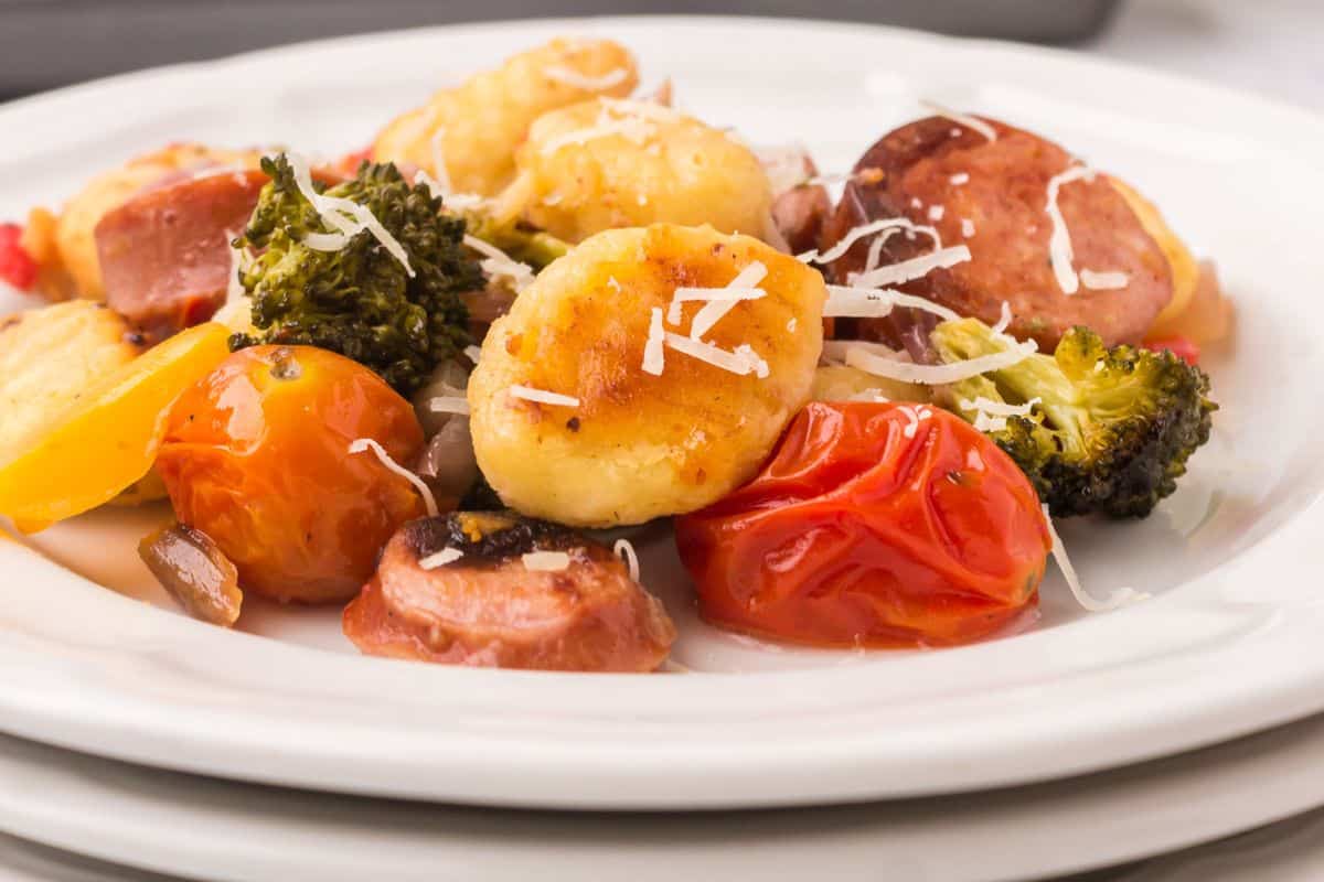 Enjoy a delicious plate of gnocchi with cherry tomatoes, broccoli, sausage slices, and grated cheese on top—an easy cleanup sheet pan meal perfect for busy nights.
