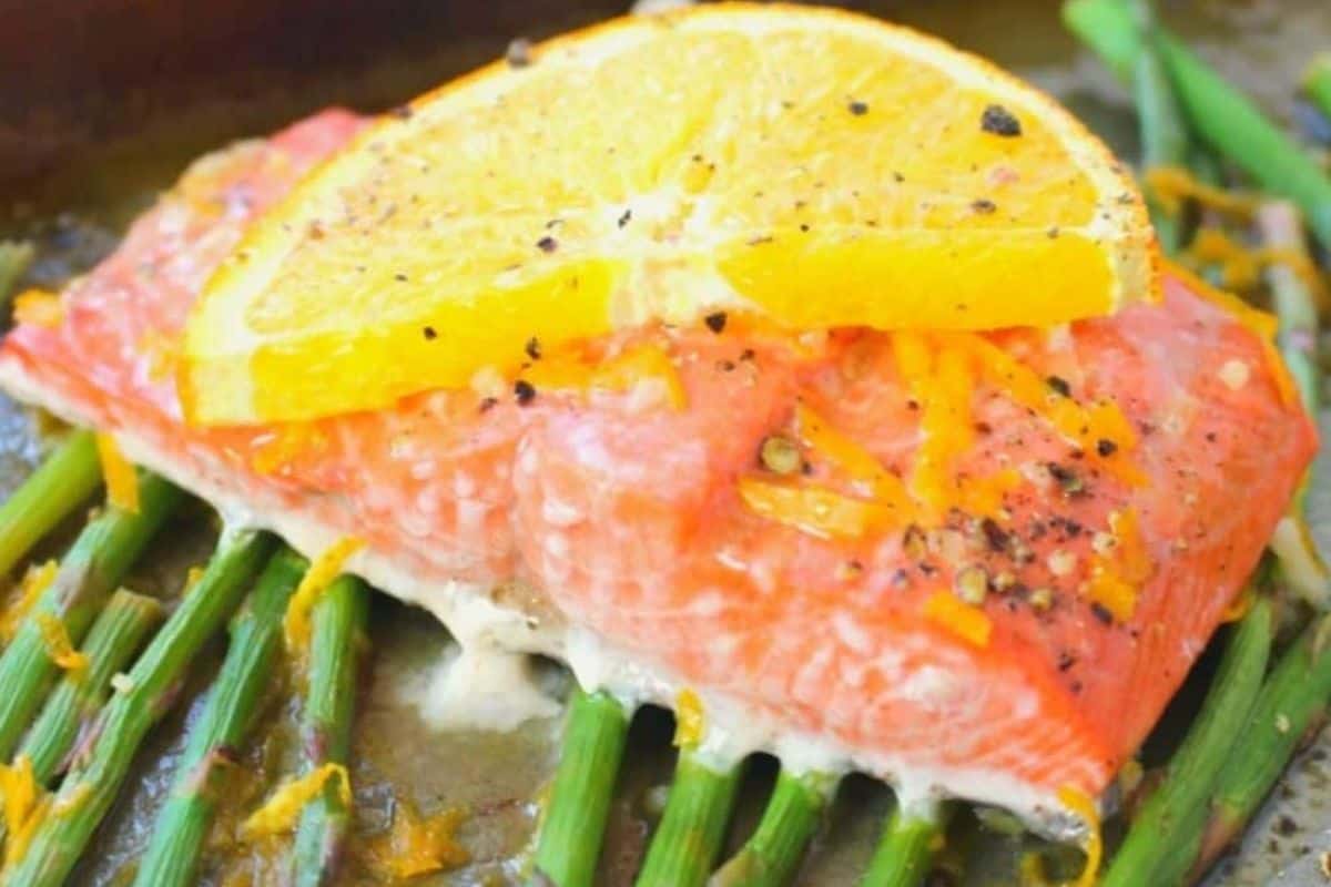Discover this irresistible salmon dish: a baked salmon fillet topped with a lemon slice, delicately seasoned with pepper, and elegantly resting on a bed of vibrant green asparagus. Perfect for those seeking delightful salmon recipes.