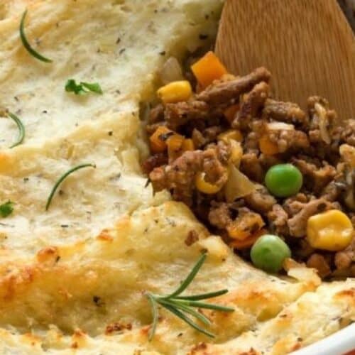 This Irish-inspired comfort food features a casserole dish crowned with mashed potatoes, unveiling a blend of minced meat and vegetables such as peas and carrots beneath. A wooden spoon rests in the dish, ready to warm your soul with every serving.