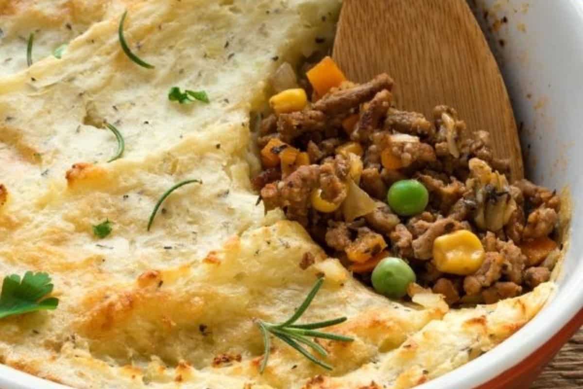 This Irish-inspired shepherds pie features a casserole dish crowned with mashed potatoes, unveiling a blend of minced meat and vegetables such as peas and carrots beneath. A wooden spoon rests in the dish, ready to warm your soul with every serving.