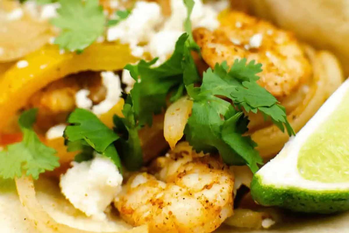 Close-up of a shrimp fajita featuring restaurant-quality grilled shrimp, sliced bell peppers, crumbled cheese, fresh cilantro, and a lime wedge on a perfectly soft tortilla.