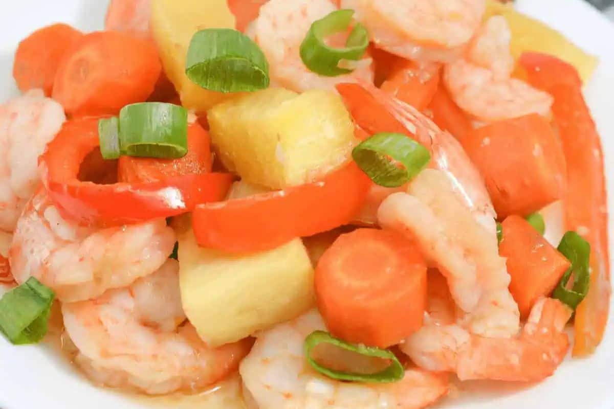 A plate of shrimp stir-fry with sliced carrots, red bell peppers, pineapple chunks, and green onions—one of our delicious recipes that promises vibrant flavors and easy cleanup.
